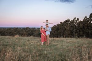 A couple stands together in a grassy field at sunset while taking outdoor engagement photos.