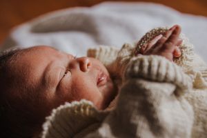 A sleeping baby wrapped in a cozy white knit blanket lies peacefully on a soft surface.