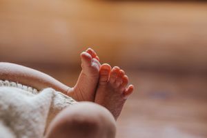 Close up of tiny newborn baby feet wrapped in soft white blanket against wooden background.