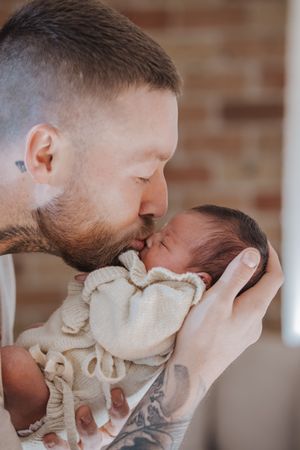 A tender moment captured in a series of photos showing a parent gently kissing a newborn against a brick wall backdrop.