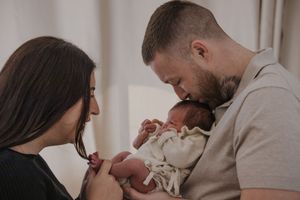 Parents sharing tender moment with their newborn baby in a softly lit room.
