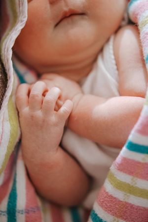 Close-up of a newborn baby's tiny fingers wrapped in a striped blanket with pink, teal and yellow colors.