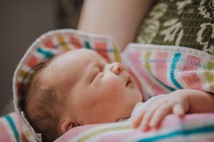 A sleeping baby wrapped in a colorful striped blanket rests peacefully in natural light.