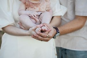Couple's hands gently hold a tiny pink baby sock in a tender pregnancy announcement moment.
