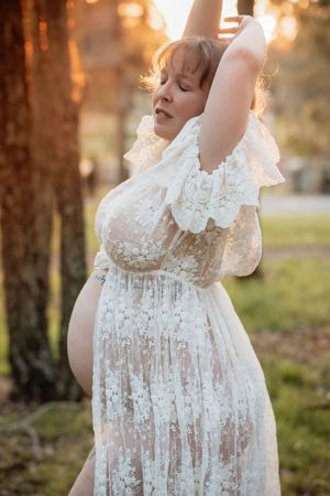 Delicate white lace maternity dress photographed in warm sunset lighting against a natural outdoor backdrop.