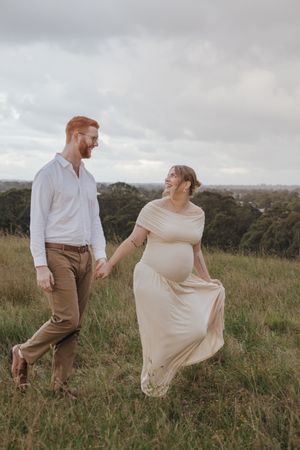 A couple dances together in a grassy field during sunset, with her cream dress flowing in the wind.