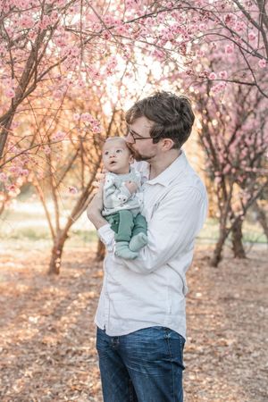A tender moment under blooming cherry blossom trees during sunset, with soft pink petals creating a dreamy backdrop.