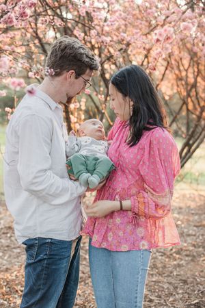 A couple stands together under blooming pink cherry blossom trees in a romantic spring photo series.