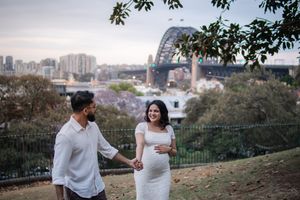 Couple shares intimate moment during outdoor maternity photography session with Sydney cityscape views.