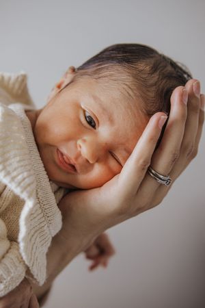 Tender newborn photography series showing baby cradled in gentle hands against neutral backdrop.