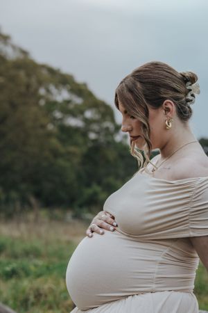 Side profile of an expectant mother in a cream dress outdoors.