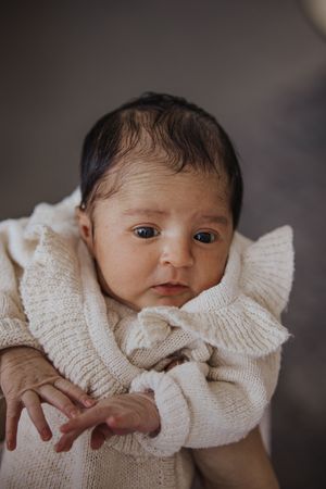 A baby wearing a cozy cream-colored knit sweater gazes at the camera with bright eyes.