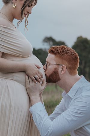 An intimate maternity photoshoot in a field shows tender moments between an expecting couple.
