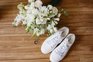 White sneakers filled with delicate white flowers and greenery arranged as decorative vases on wooden surface.