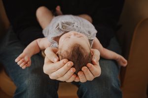 Close-up of tiny newborn baby feet being gently held in adult hands against dark background.