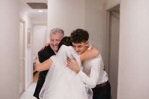 Two people help carry a white wedding dress down a hallway in an emotional moment.