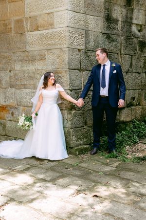 A romantic sequence of wedding photos showing a couple in formal attire interacting playfully against a stone wall backdrop.
