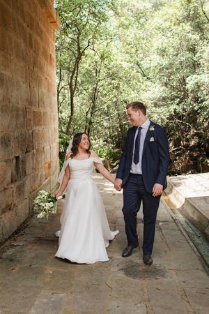 A couple shares playful moments in a stone archway walkway surrounded by greenery during their wedding photo session.