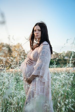 A woman in a flowing white dress stands thoughtfully among wildflowers in a dreamy outdoor setting.