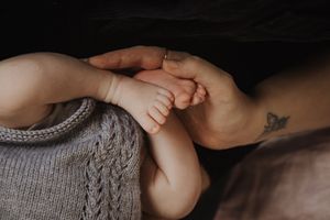 A baby's tiny feet being gently held by adult hands in a warm, intimate setting.