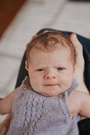 A newborn baby wearing a soft gray knitted sweater makes various adorable expressions in a series of close-up photos.