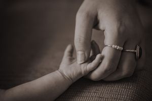 Delicate hands tenderly cradle and support a sleeping newborn baby in monochromatic lighting.