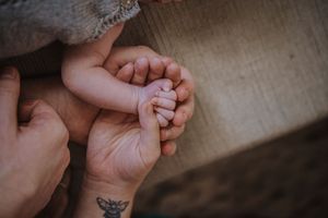 Close-up photo of hands holding and caressing a newborn baby's tiny feet with a delicate butterfly tattoo visible.