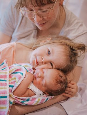 A tender moment showing two young children cuddling together while being embraced in a warm, intimate setting.