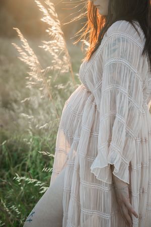 Ethereal white lace dress catches golden sunlight in a field of swaying summer grasses at sunset.