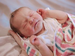 A peaceful sleeping newborn baby wearing a colorful striped outfit rests on white bedding.