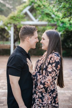 A couple shares intimate moments in a garden setting while wearing black and floral outfits.