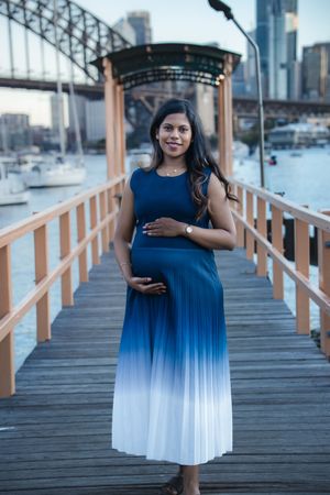 Beautiful maternity photoshoot on a wooden pier with a blue ombre dress against an urban waterfront backdrop.
