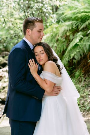 A tender moment between newlyweds embracing in a lush garden setting with ferns and greenery.