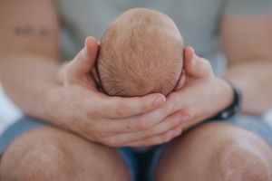 Close-up shot of hands holding a small newborn baby wrapped in a soft blanket.