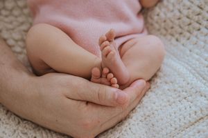 Adult hands gently holding tiny baby feet on soft knitted blanket in tender moment.
