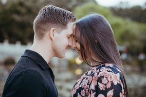 A romantic couple in formal attire embraces outdoors during a photo session at sunset.