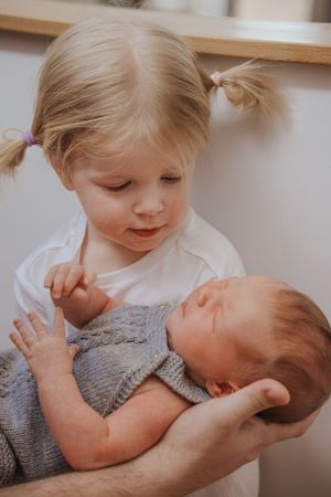 A tender moment between siblings as a young child gently holds and gazes at a newborn baby.