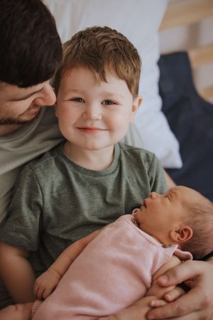 A young child in a green shirt looks lovingly at a baby in a pink outfit resting in someone's arms.