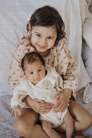 Siblings sharing sweet moments on white bedding with soft natural lighting.