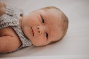 A series of soft, dreamy photos showing a baby wearing a knitted gray sweater lying on white bedding.
