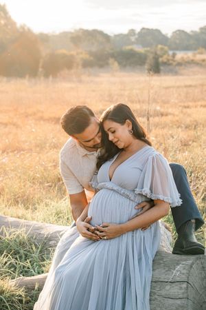 A couple embraces in a golden field during sunset as they share an intimate maternity photoshoot moment.