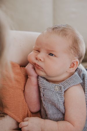 Sleeping newborn baby wearing gray knit sweater lying on orange cushion in soft natural light.