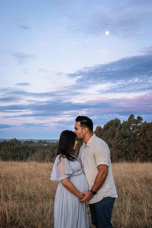 A couple shares a romantic moment at sunset in a golden field with trees in the background.