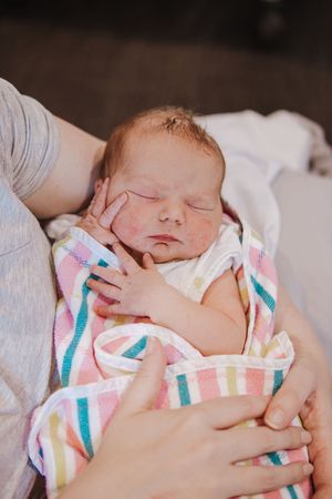 A newborn baby sleeping peacefully in a striped blanket with pink and turquoise colors.