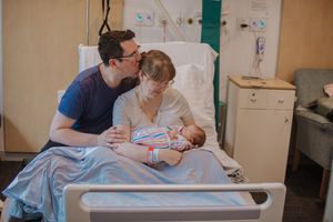 A newborn baby rests in a hospital bed while being cared for by medical staff in a healthcare setting.