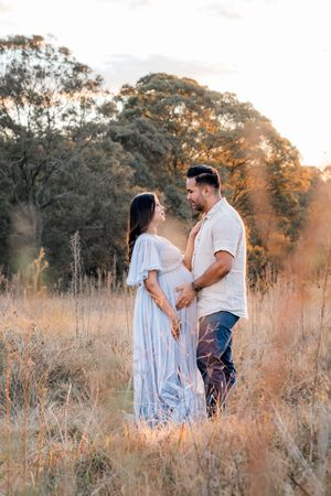 A couple shares tender moments in a golden sunlit field of tall grass during sunset.