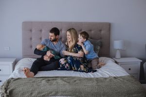Family relaxing together on a gray bed, wearing casual blue clothing while sharing a playful moment.