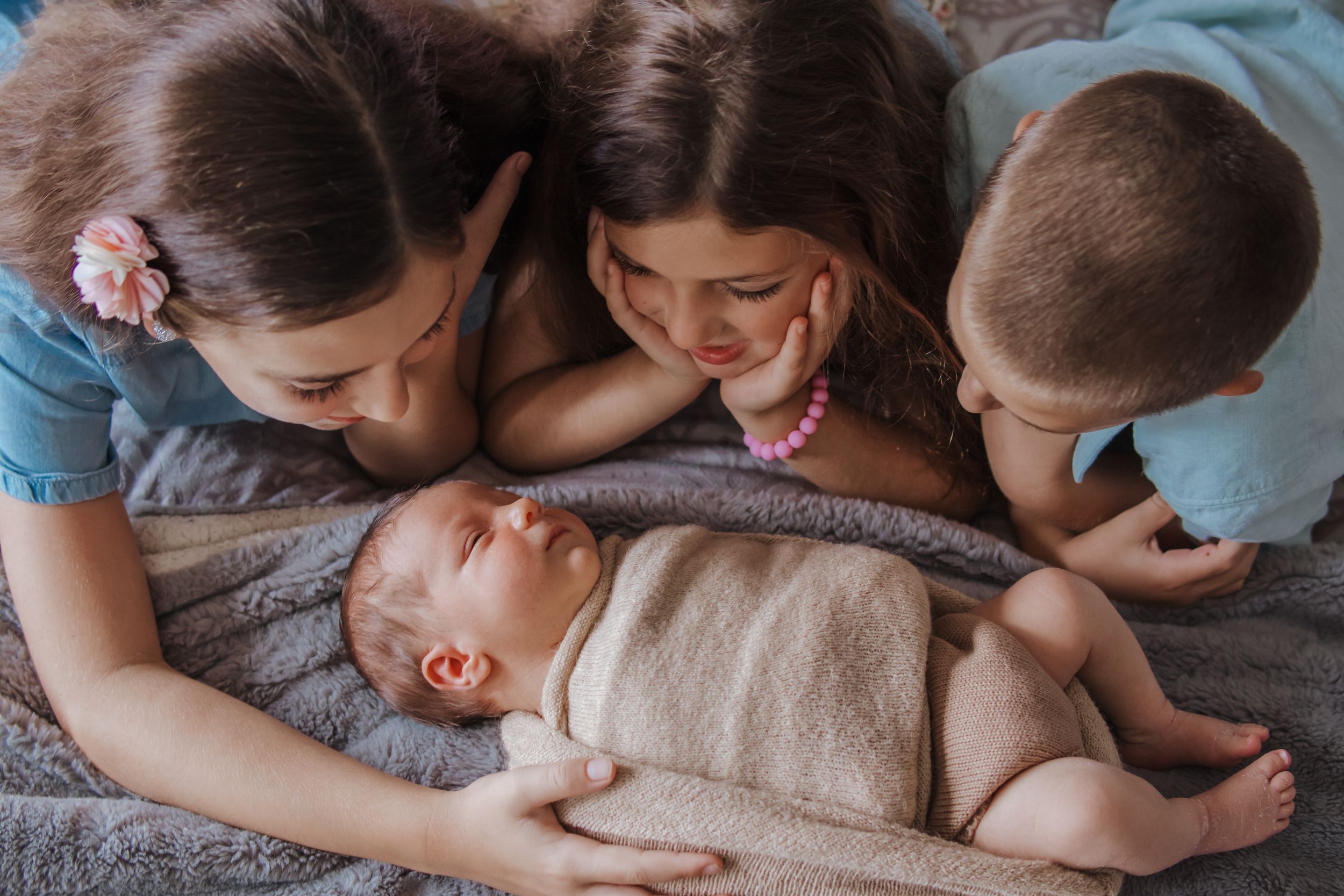 Family members lovingly gather around a baby wrapped in a beige blanket lying on a gray surface.