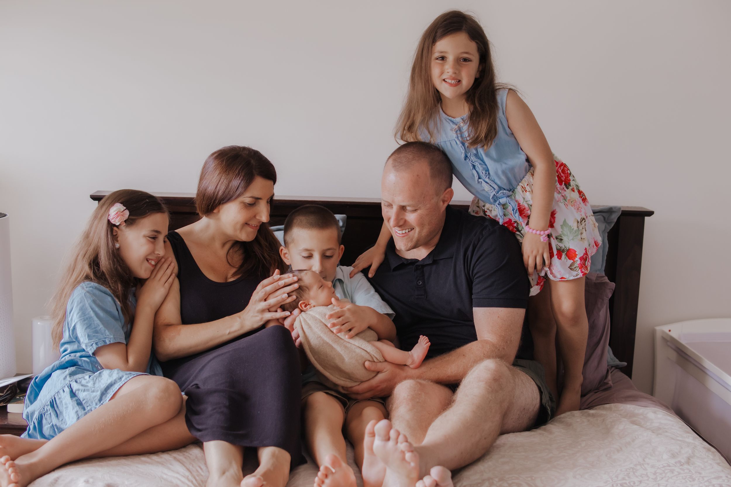 A family relaxes together on a cozy bed, sharing smiles and tender moments in casual attire.
