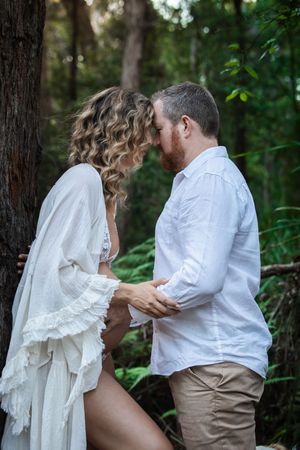 A couple in white and khaki attire share an intimate moment during a woodland photo session.